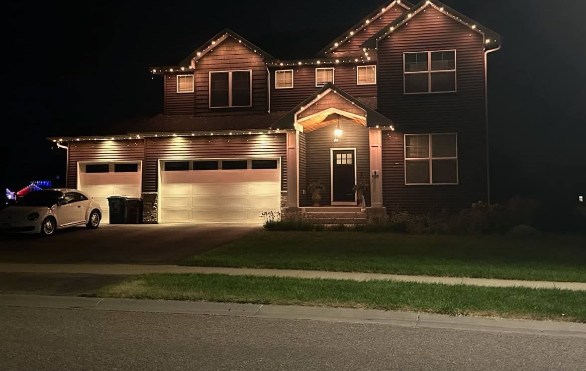 Two-story home at night with warm white lights running along every roofline and the garage eaves